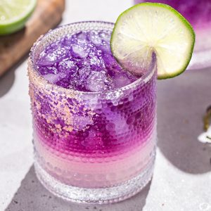 Close up of a Galaxy Margarita with another purple margarita and a lime in the background.