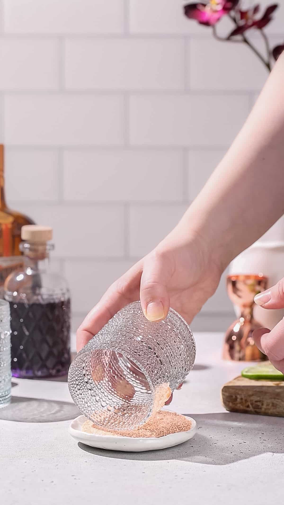 Hand dipping a cocktail glass into a dish of salt to make the salt rim.