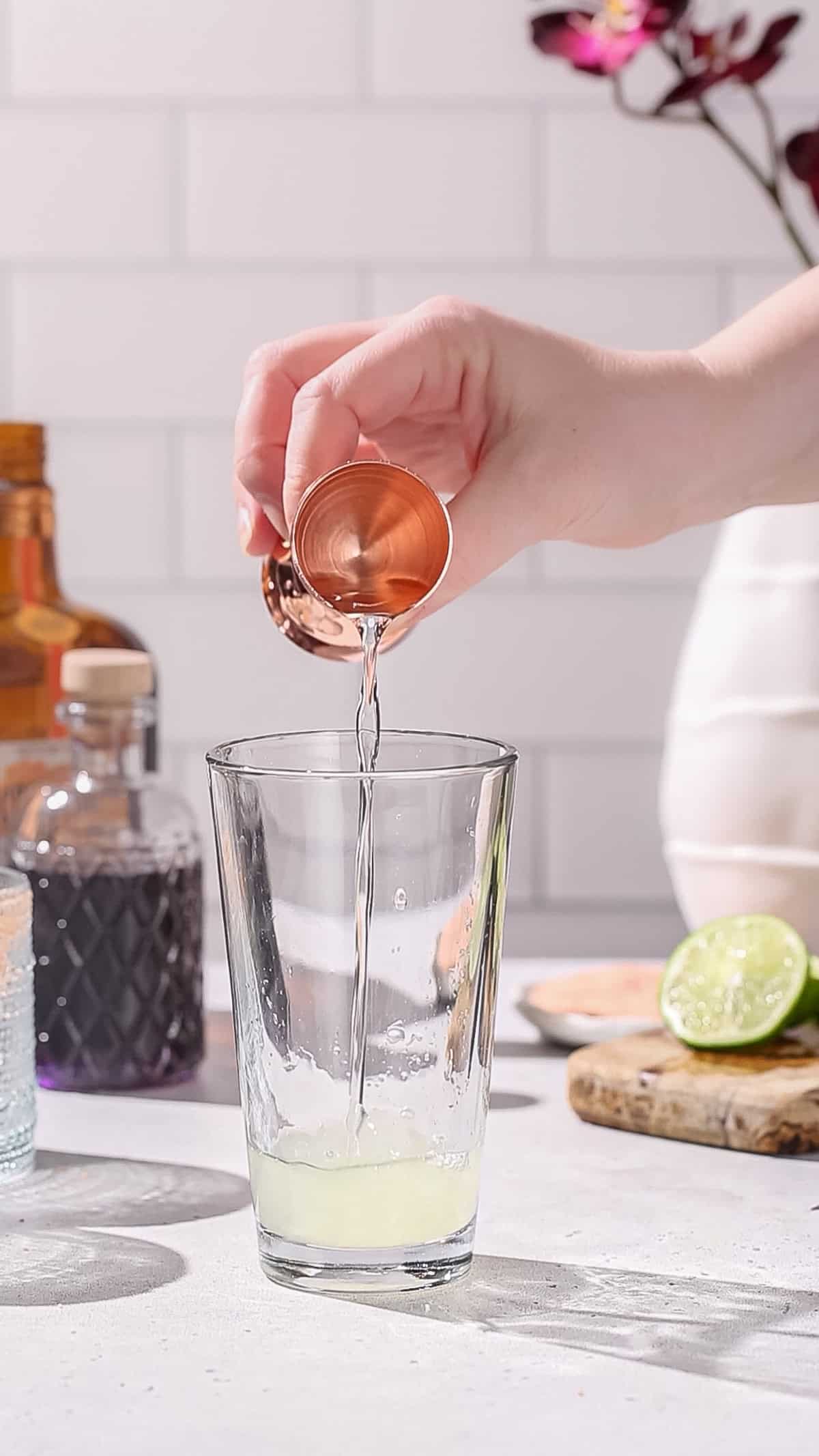 Hand adding clear liquid to a cocktail shaker.