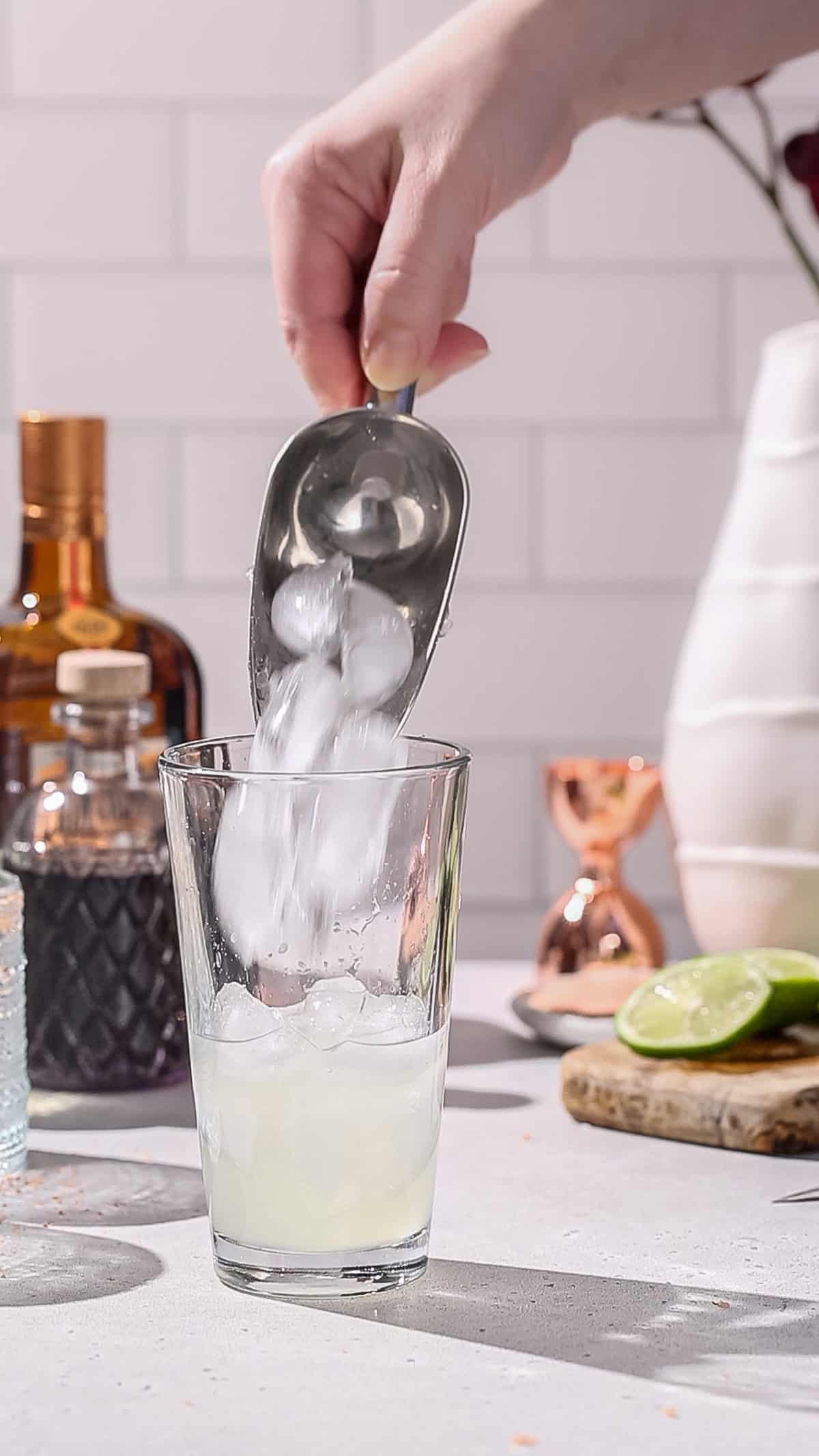 Hand adding ice to a cocktail shaker.