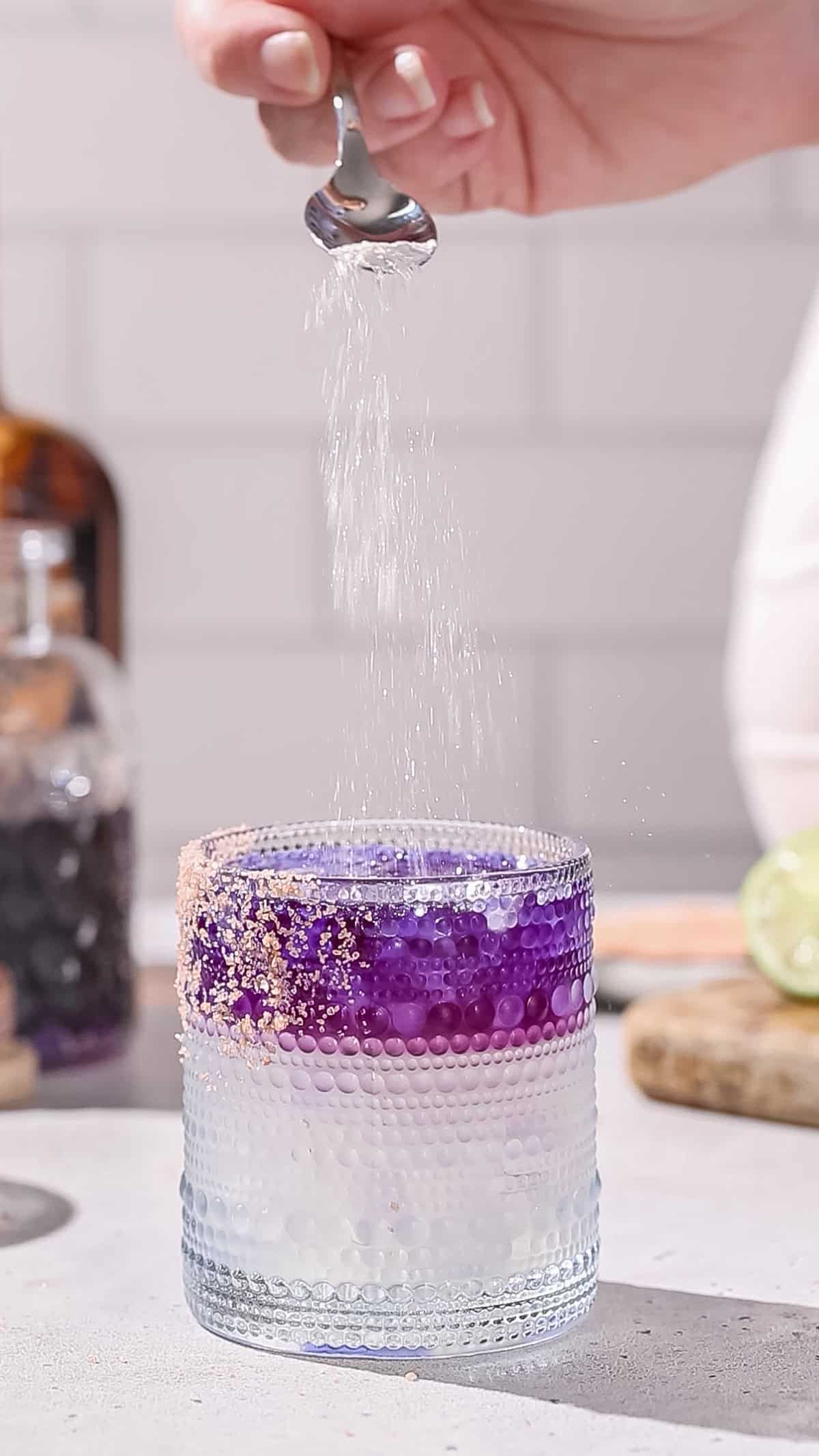 Hand sprinkling edible glitter onto a cocktail.