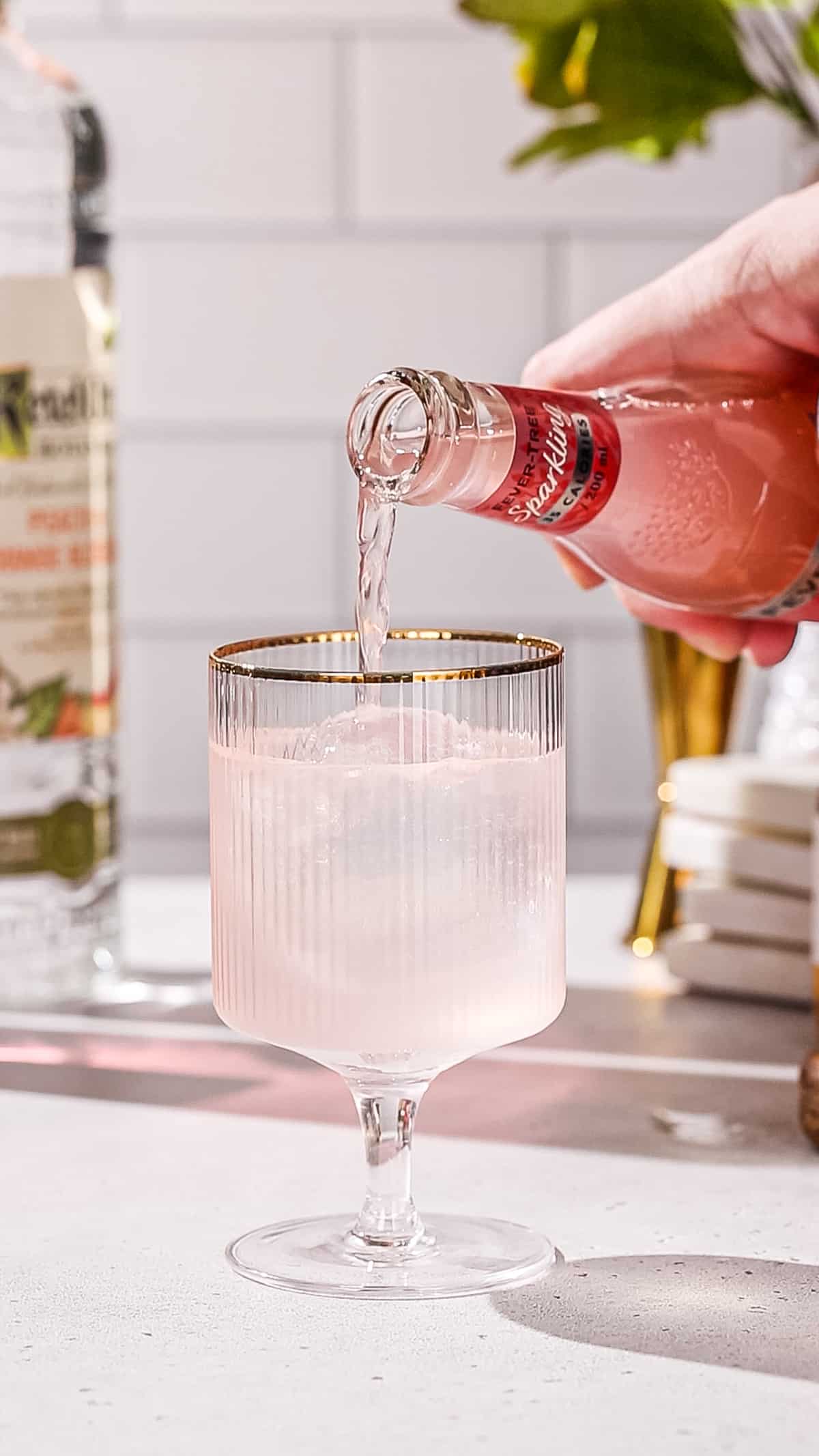 Hand pouring grapefruit soda into a cocktail glass.