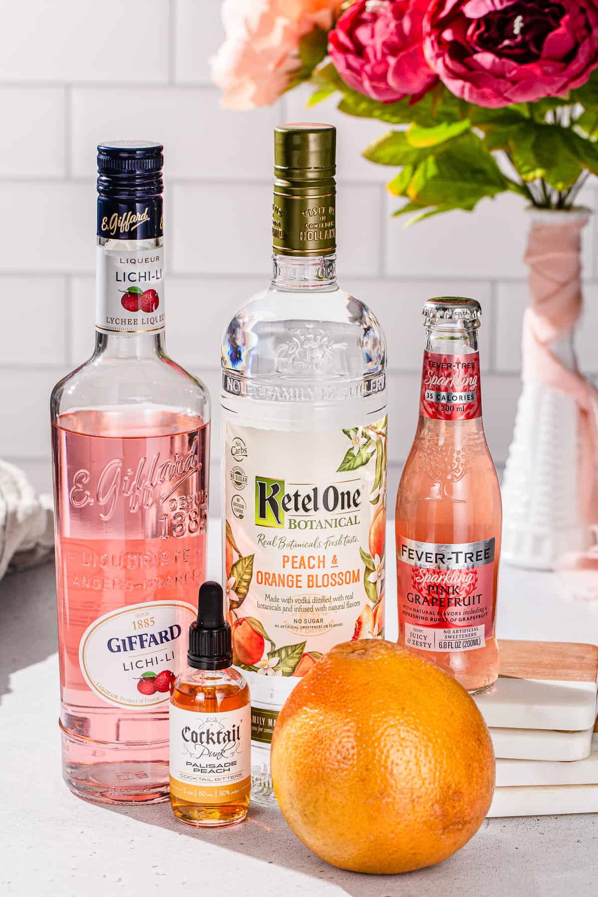 Ingredients to make a Grapefruit and Peach Vodka cocktail together on a countertop.