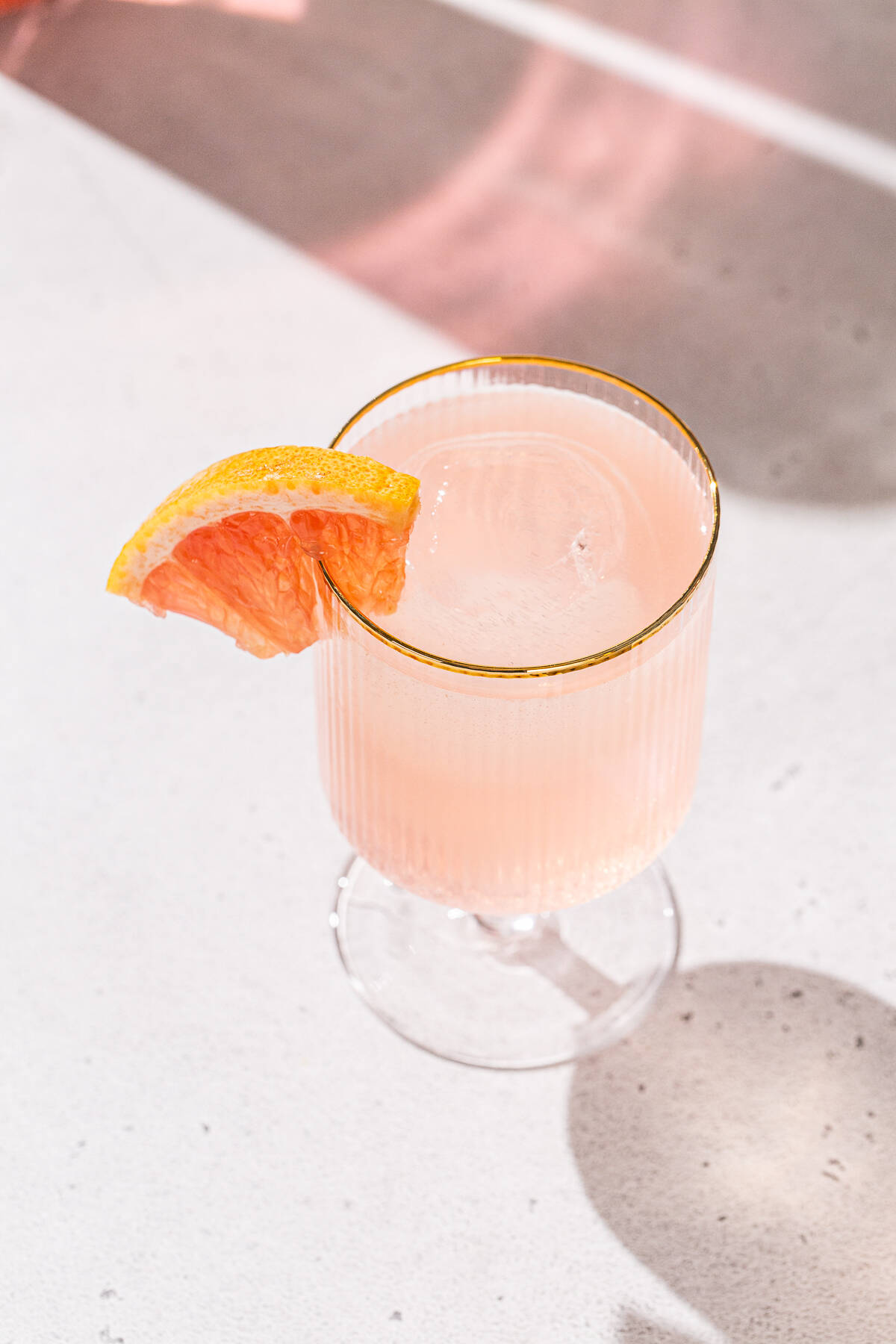 Overhead view of a gold-rimmed cocktail glass containing a peach and grapefruit cocktail, with a piece of grapefruit as the garnish.