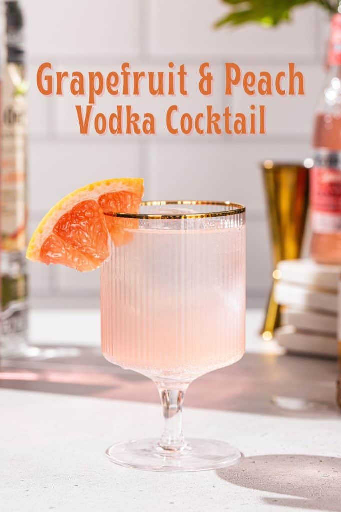 Side view of a Grapefruit Peach vodka cocktail, with a grapefruit wedge as a garnish, in a gold-rimmed glass. Text above the drink says “Grapefruit & Peach Vodka Cocktail”.