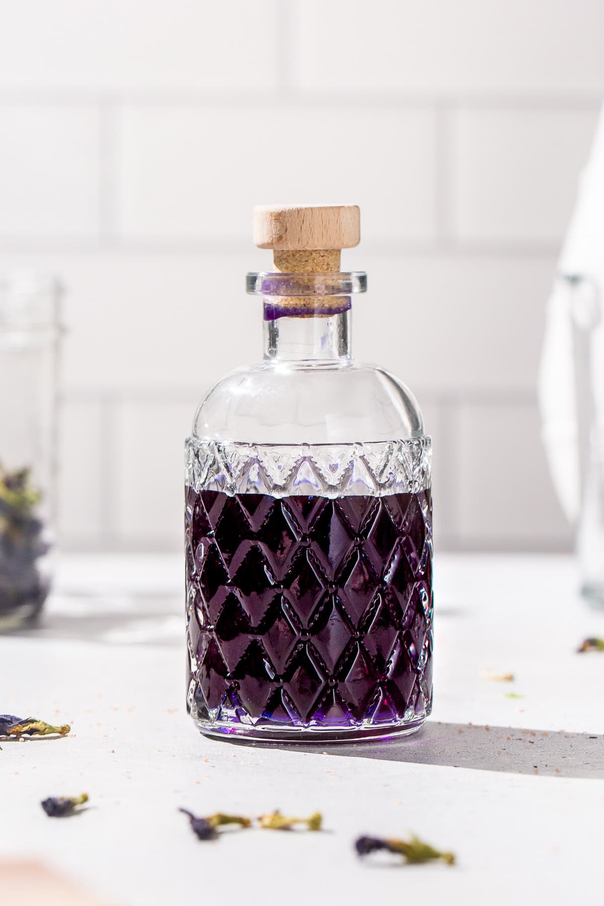 Close up of a bottle of purple butterfly pea tequila on a white countertop.