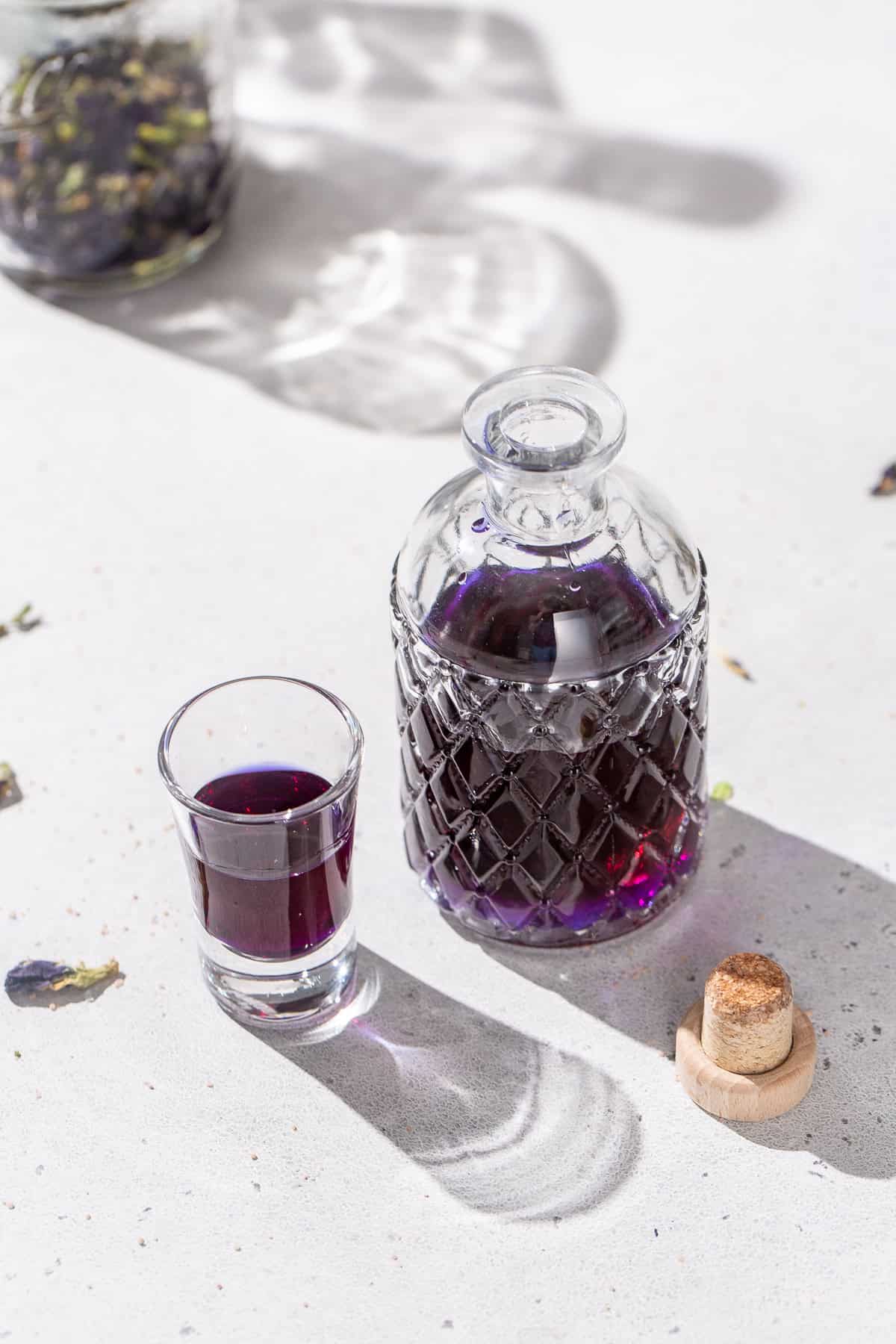 An open bottle of butterfly pea tequila with a shot glass next to it filled with the same purple liquid.