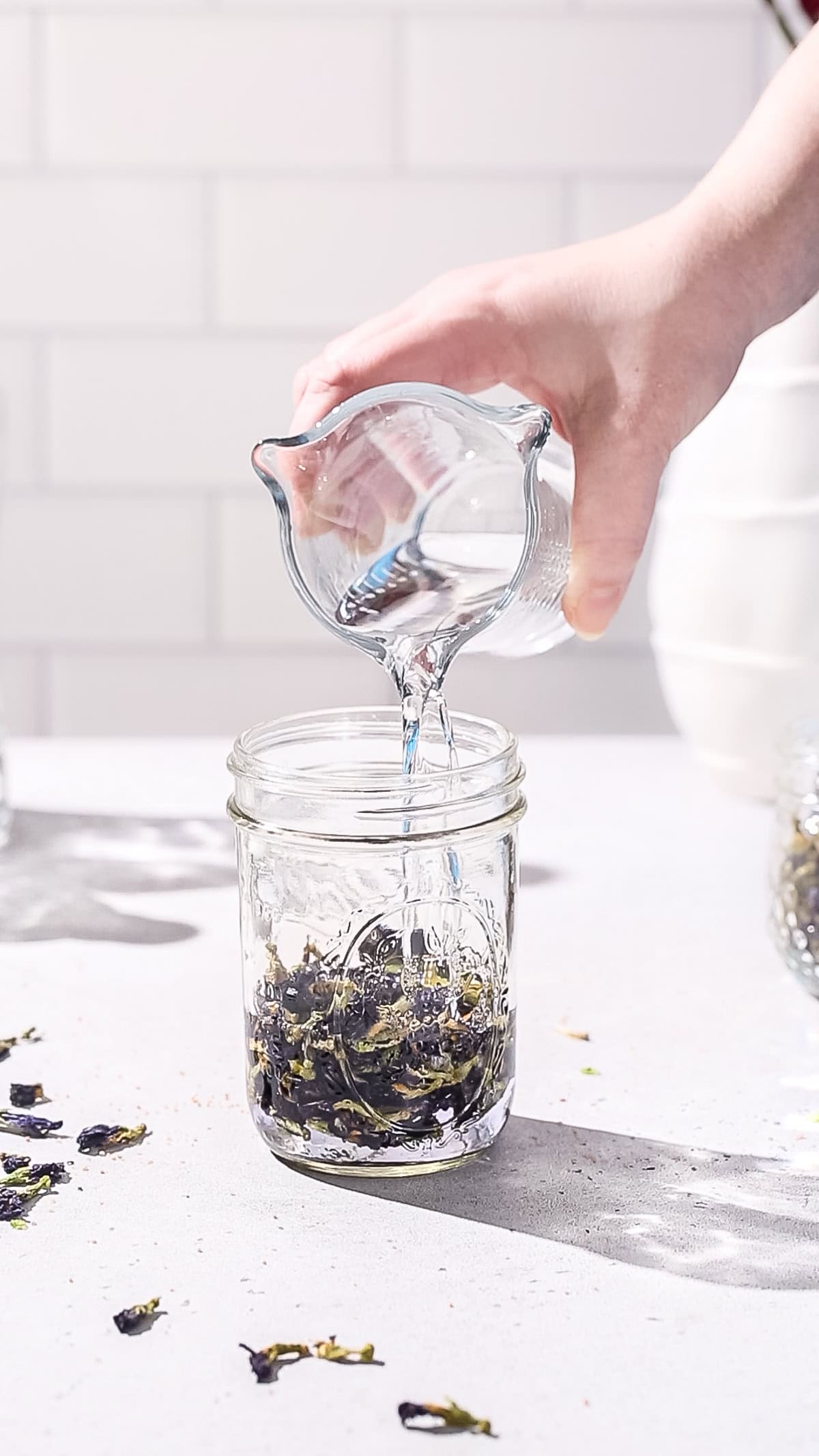 Hand adding tequila to a jar of butterfly pea flowers.