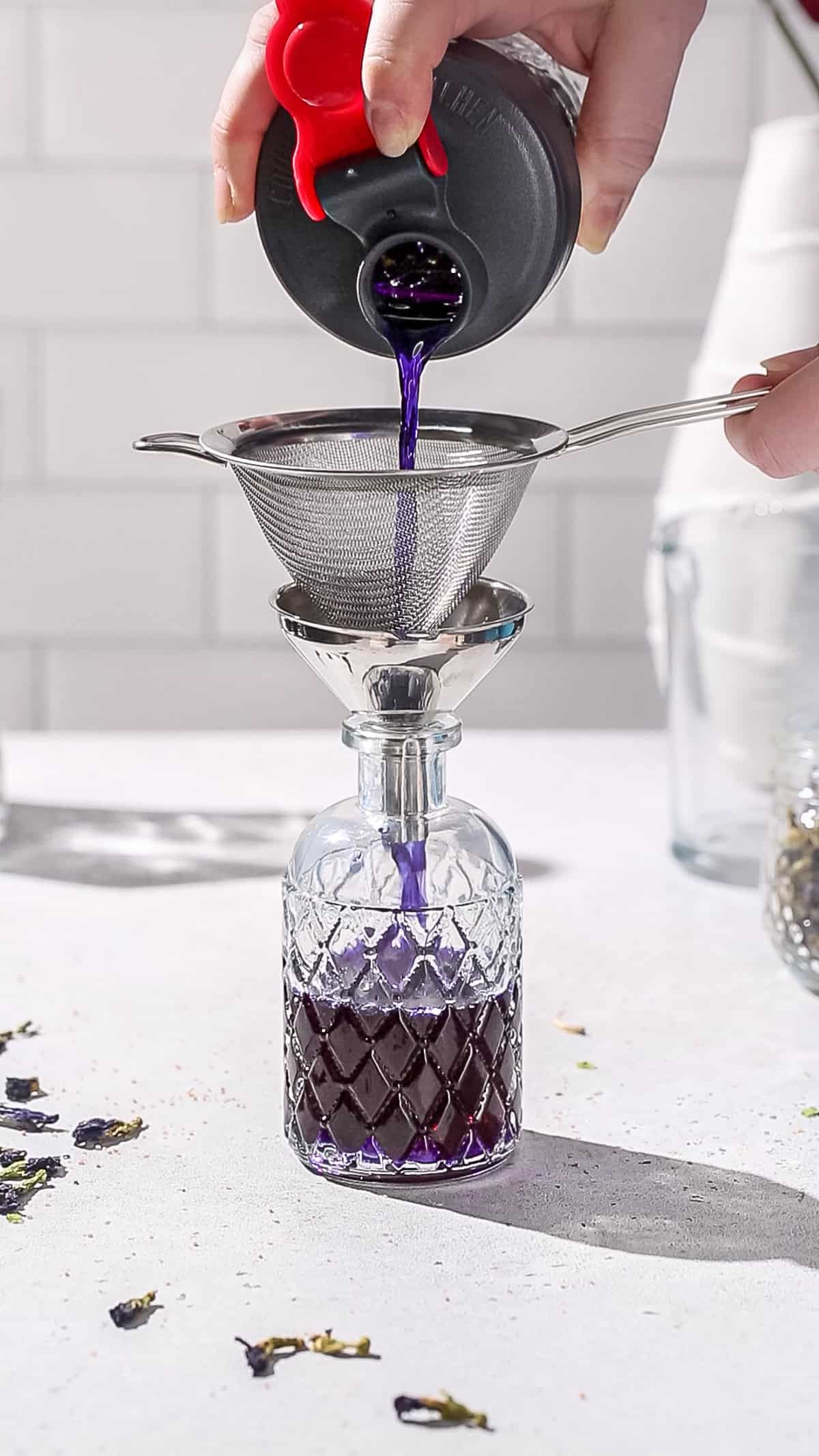 Hands straining and funneling purple liquid into a glass bottle.