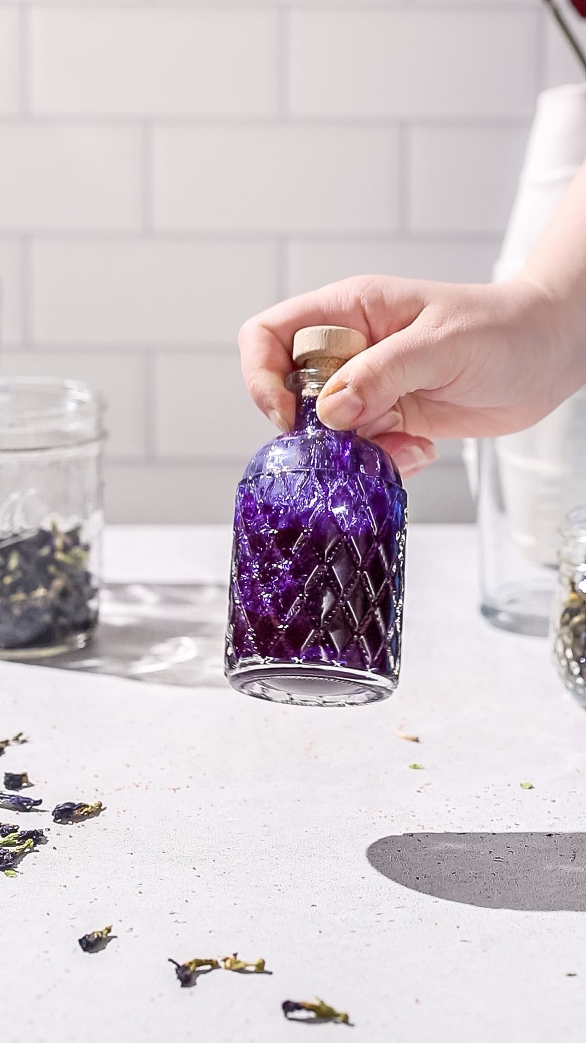 Hand picking up a glass bottle filled with dark purple liquid