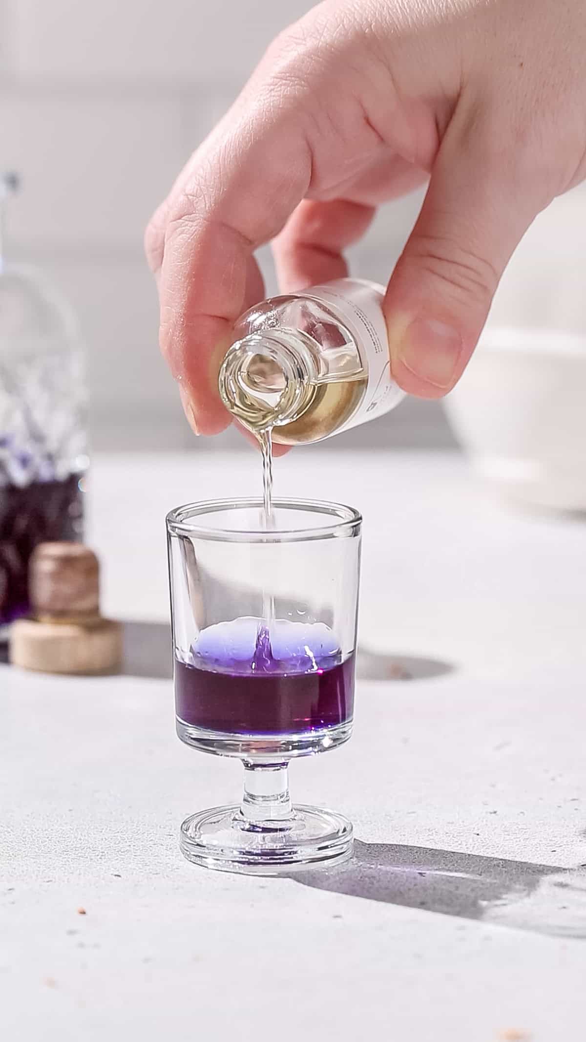 Hand pouring lime acid solution into a shot glass filled with purple liquid.