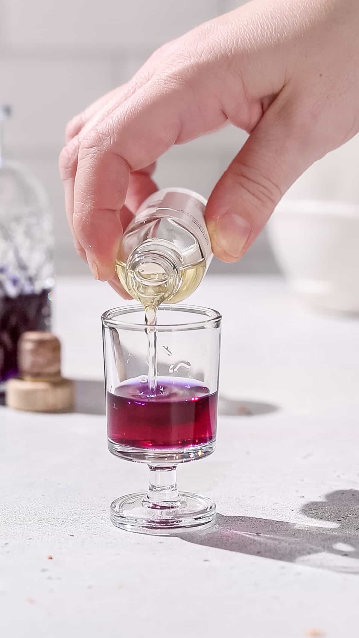 Hand pouring lime acid solution into a shot glass filled with dark pink liquid.