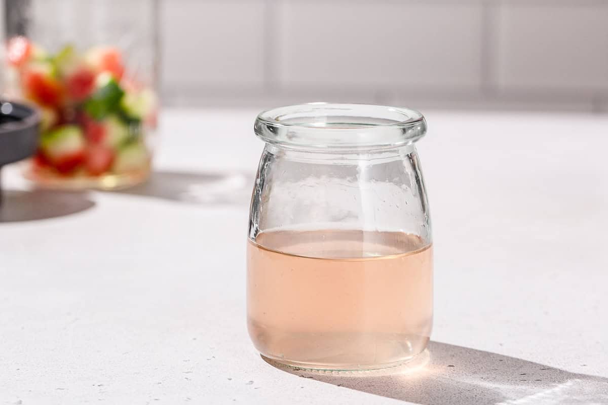 A jar of watermelon rind syrup with some watermelon rinds in the background.