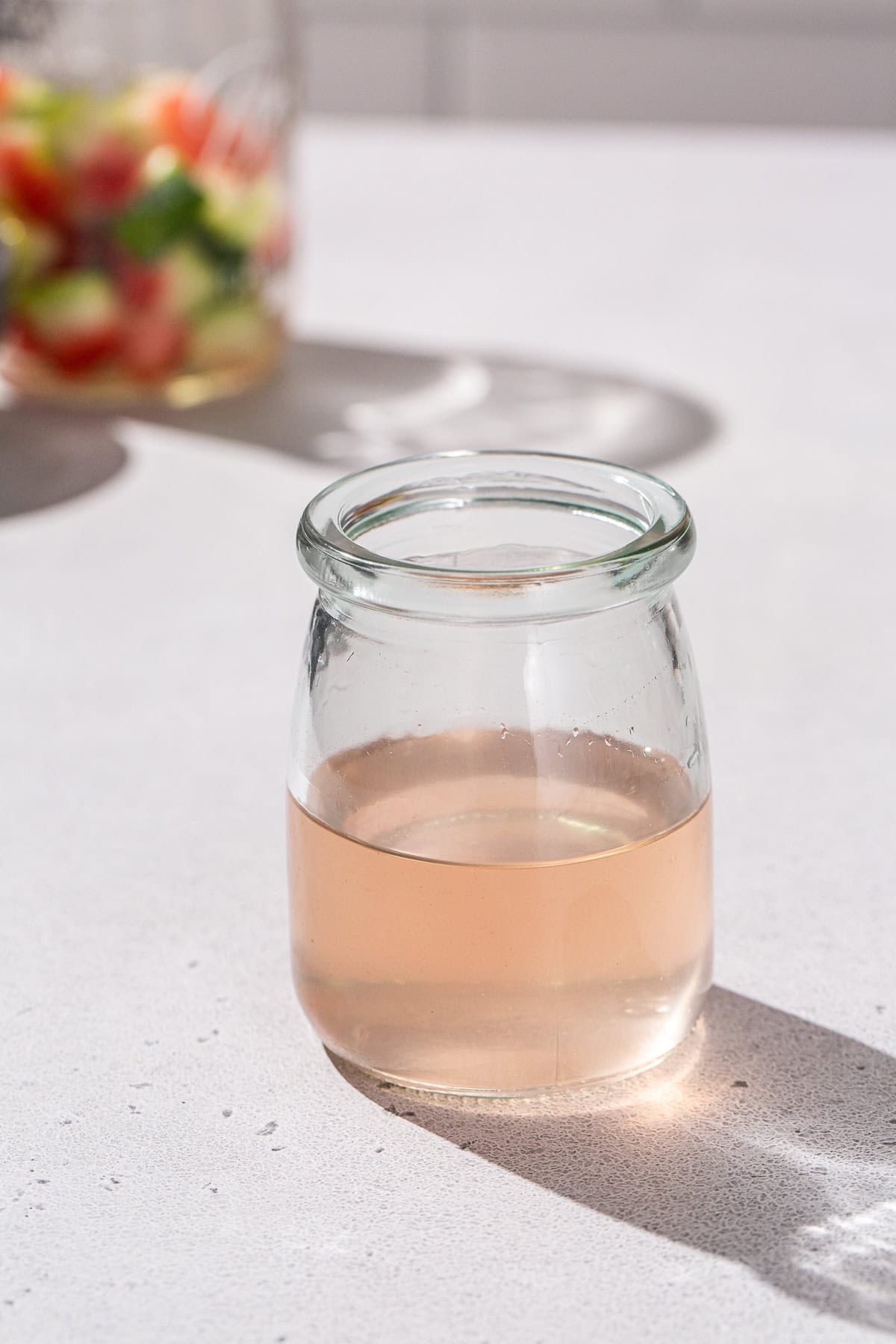 A jar of watermelon rind syrup with some watermelon rinds in the background.