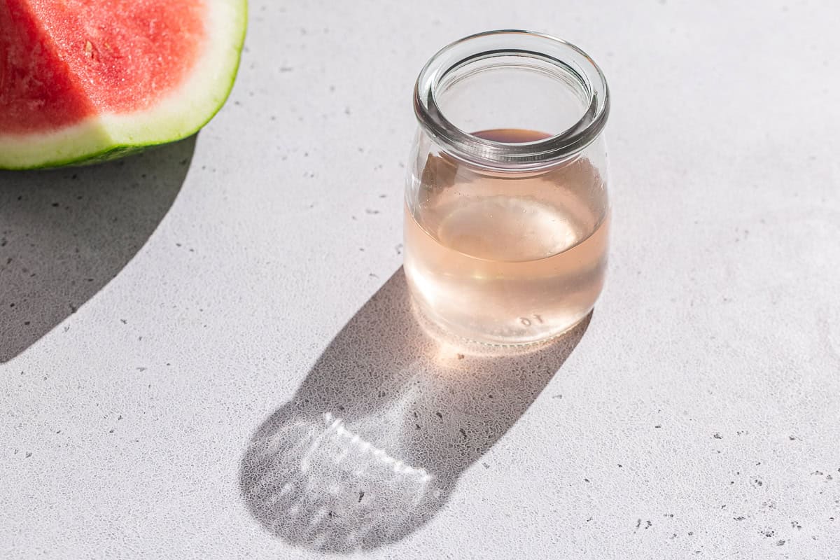 A watermelon next to a jar of watermelon rind syrup.