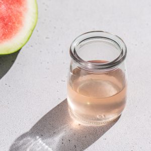 A watermelon next to a jar of watermelon rind syrup.