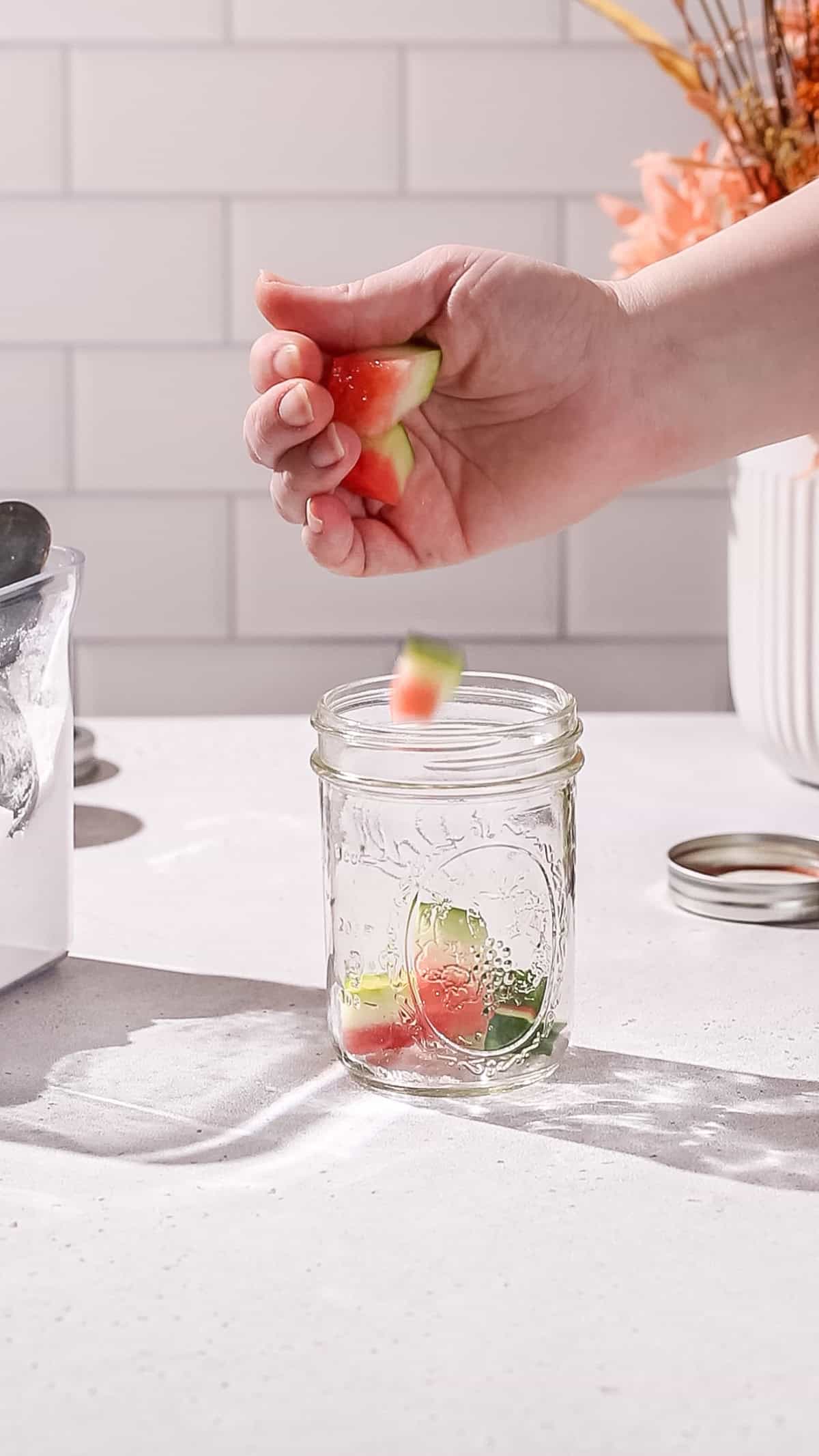 Hand adding watermelon rind chunks to a jar.