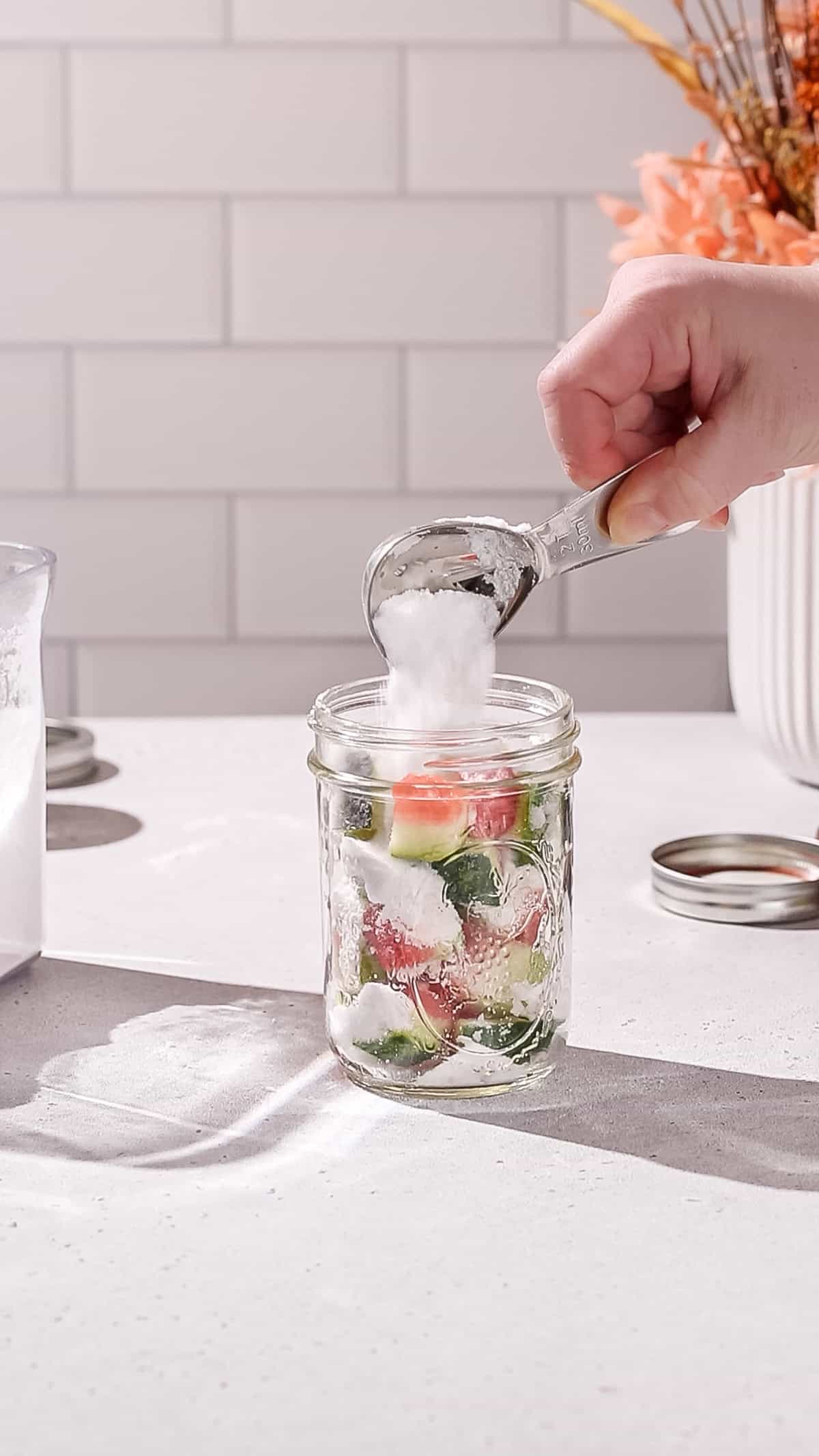 Hand adding sugar to a jar filled with watermelon rinds.