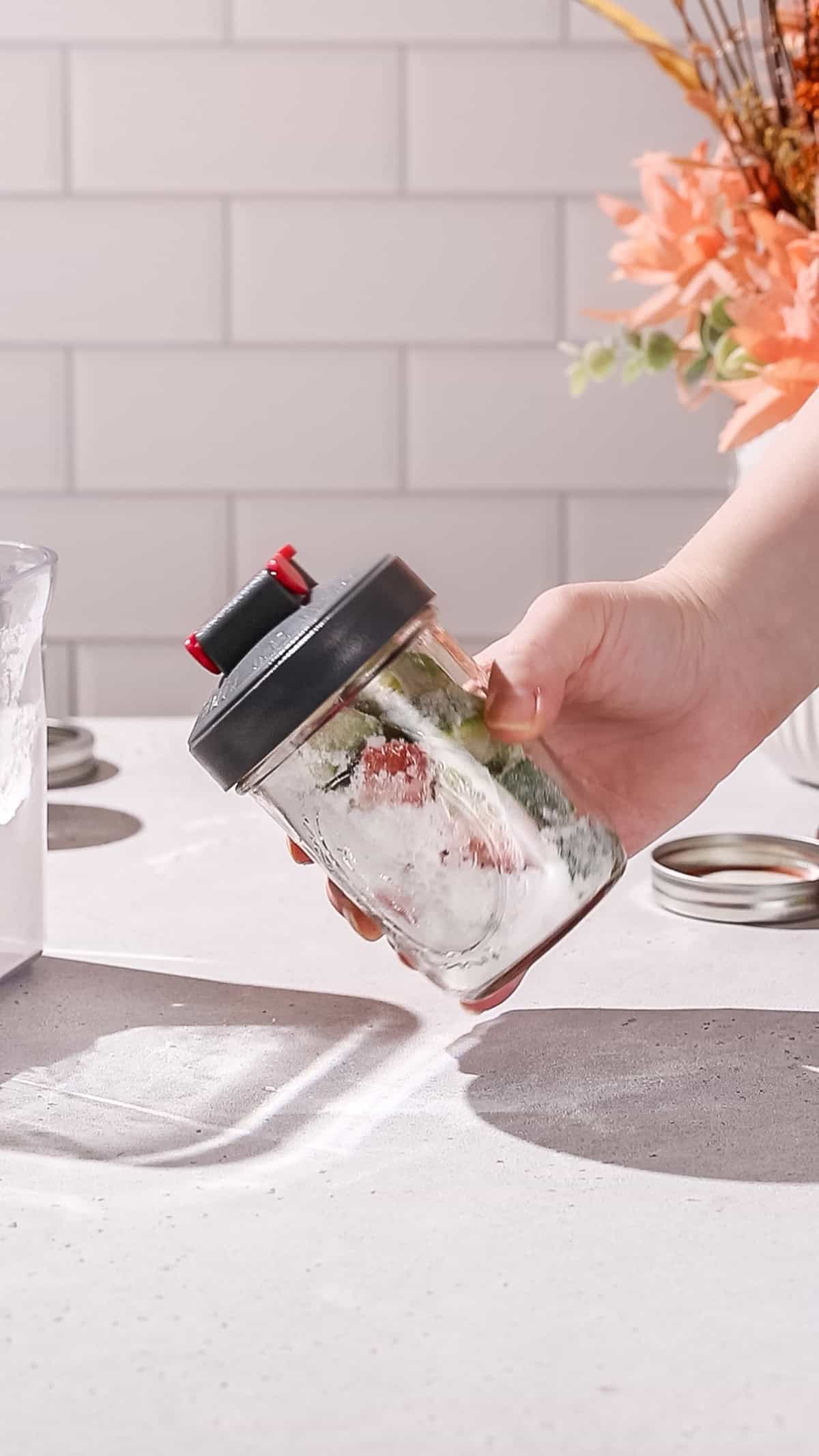 Hand shaking a sealed jar with watermelon rinds and sugar in it.