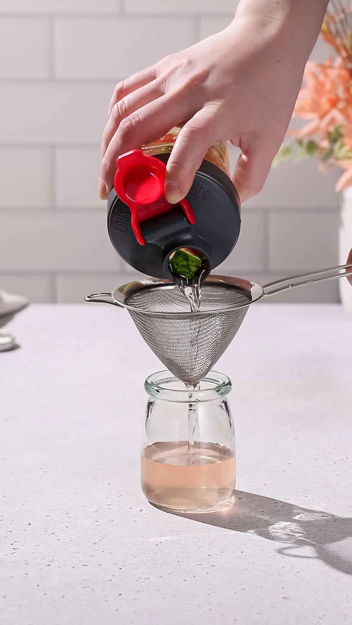 Hand straining watermelon rind syrup into a jar.