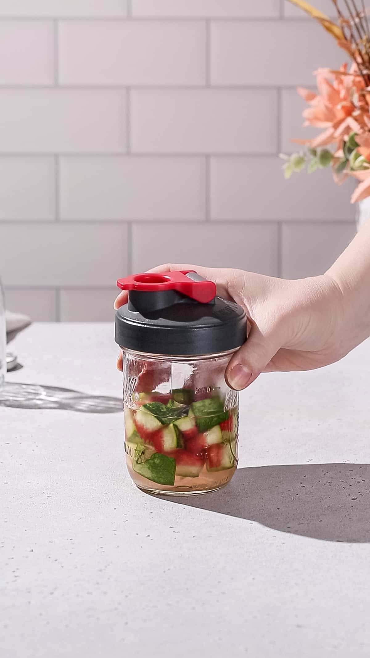 Hand holding a jar filled with watermelon rinds and syrup.