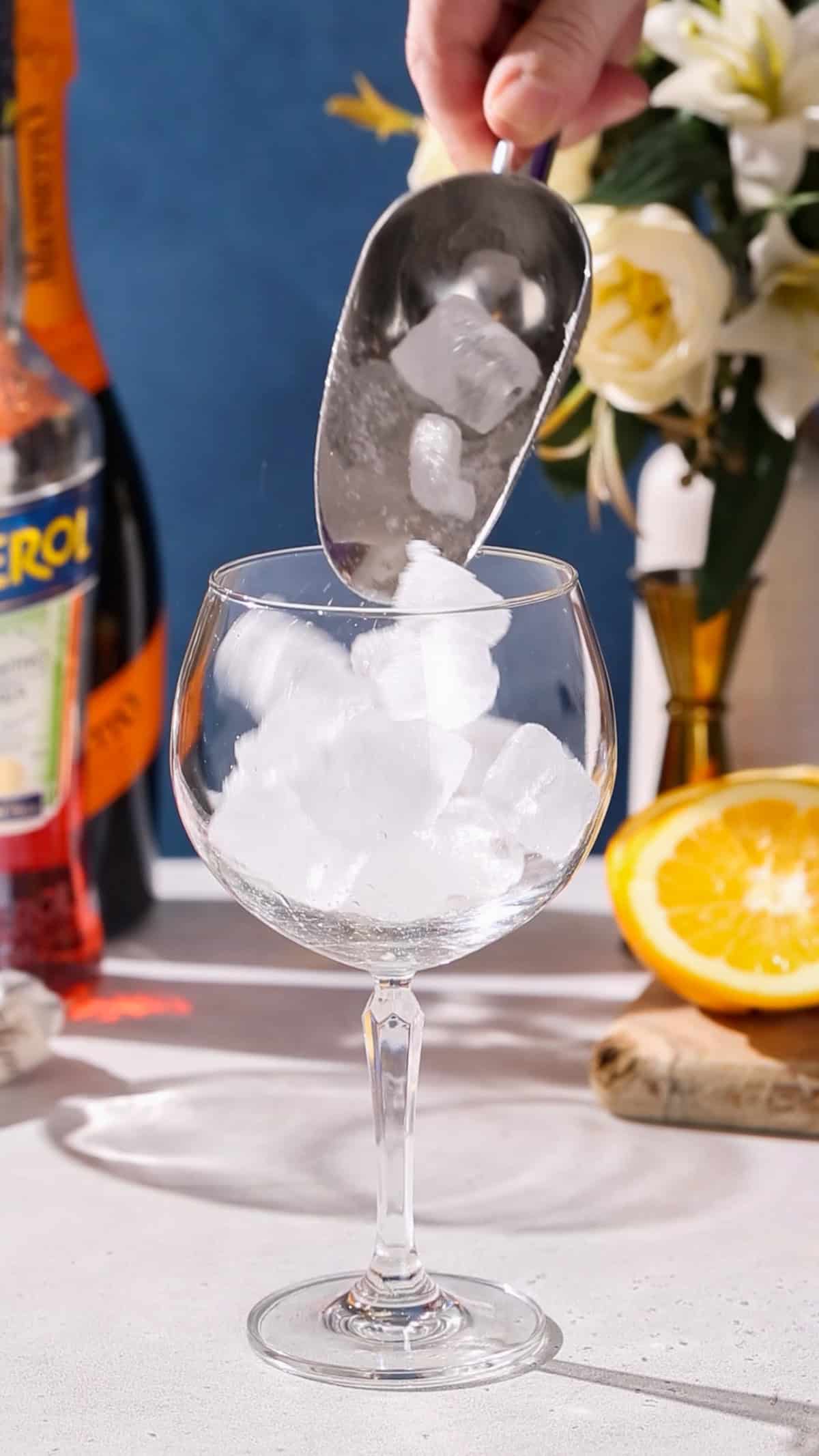 Hand using an ice scoop to add ice to a stemmed cocktail glass.