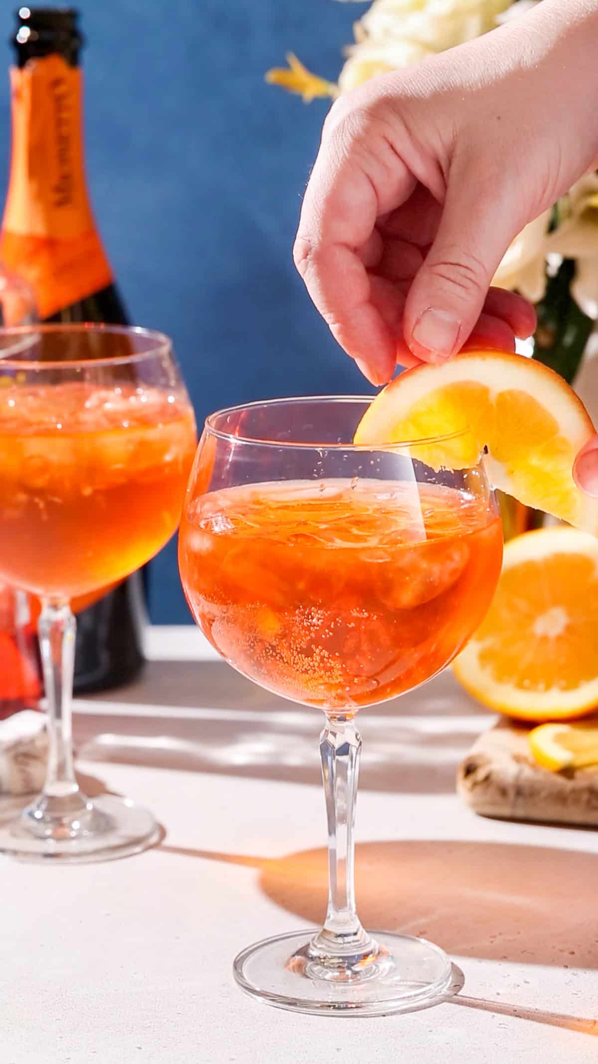 Hand adding an orange slice garnish to a spritz cocktail.