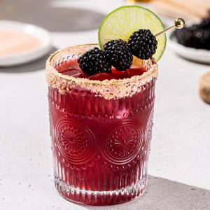 Blackberry Margarita tequila cocktail on a countertop. It is garnished with blackberries and a lime slice.