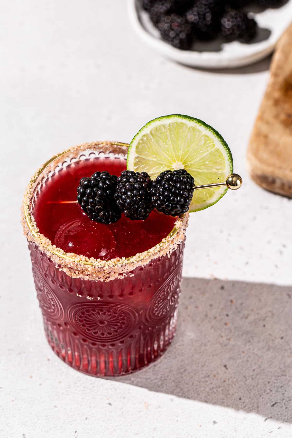 Overhead view of a Blackberry Margarita cocktail. The drink is in an old fashioned cocktail glass and garnished with fresh blackberries and a lime slice.