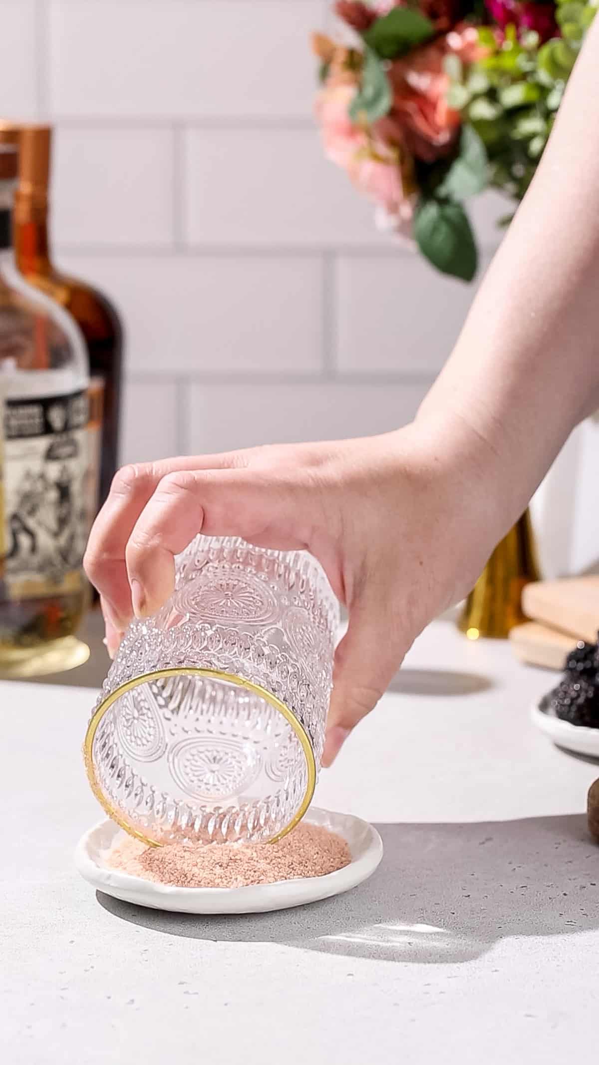 Hand dipping the rim of a cocktail glass into a dish of Himalayan salt.