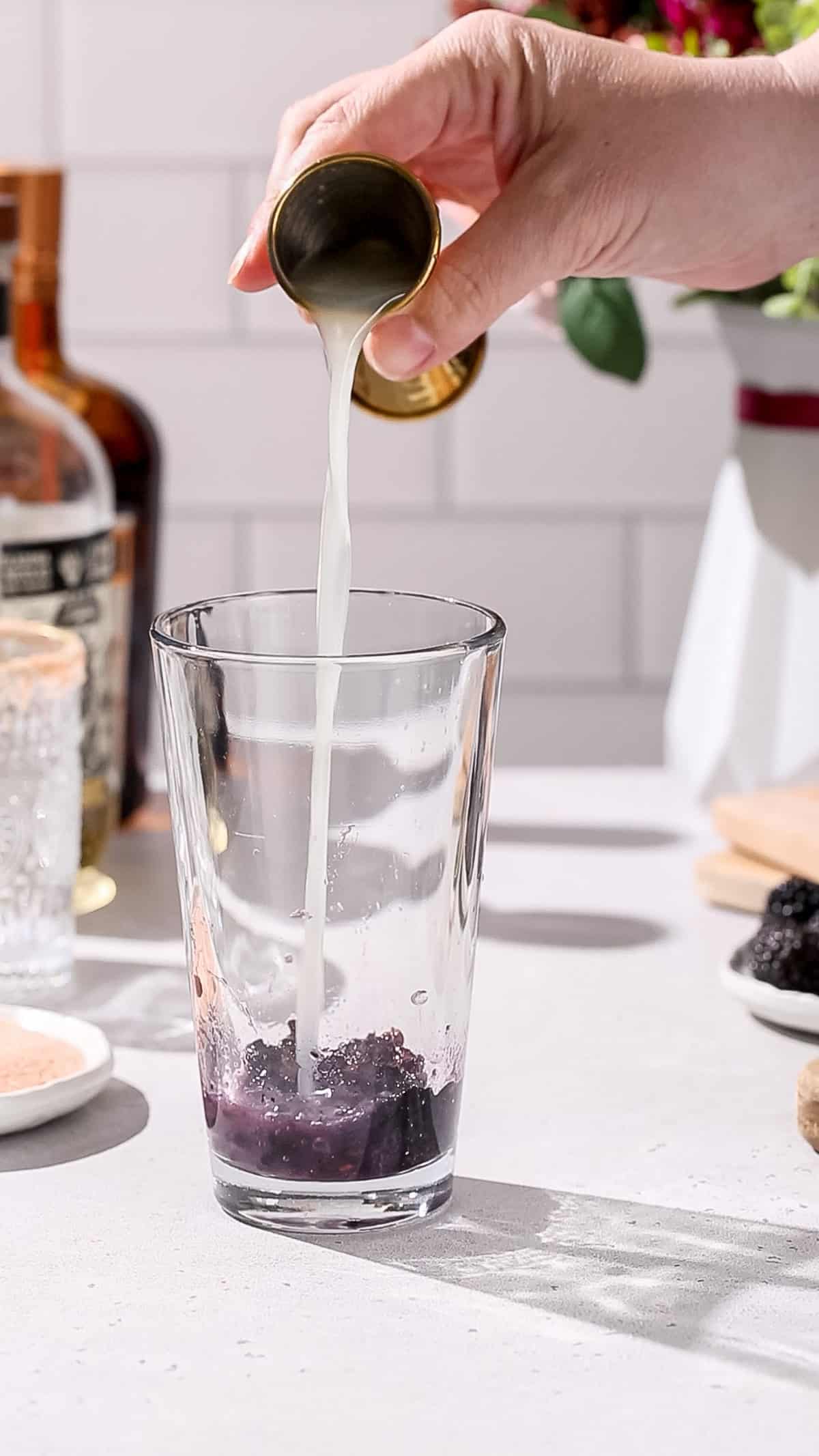 Hand pouring lime juice into a cocktail shaker.