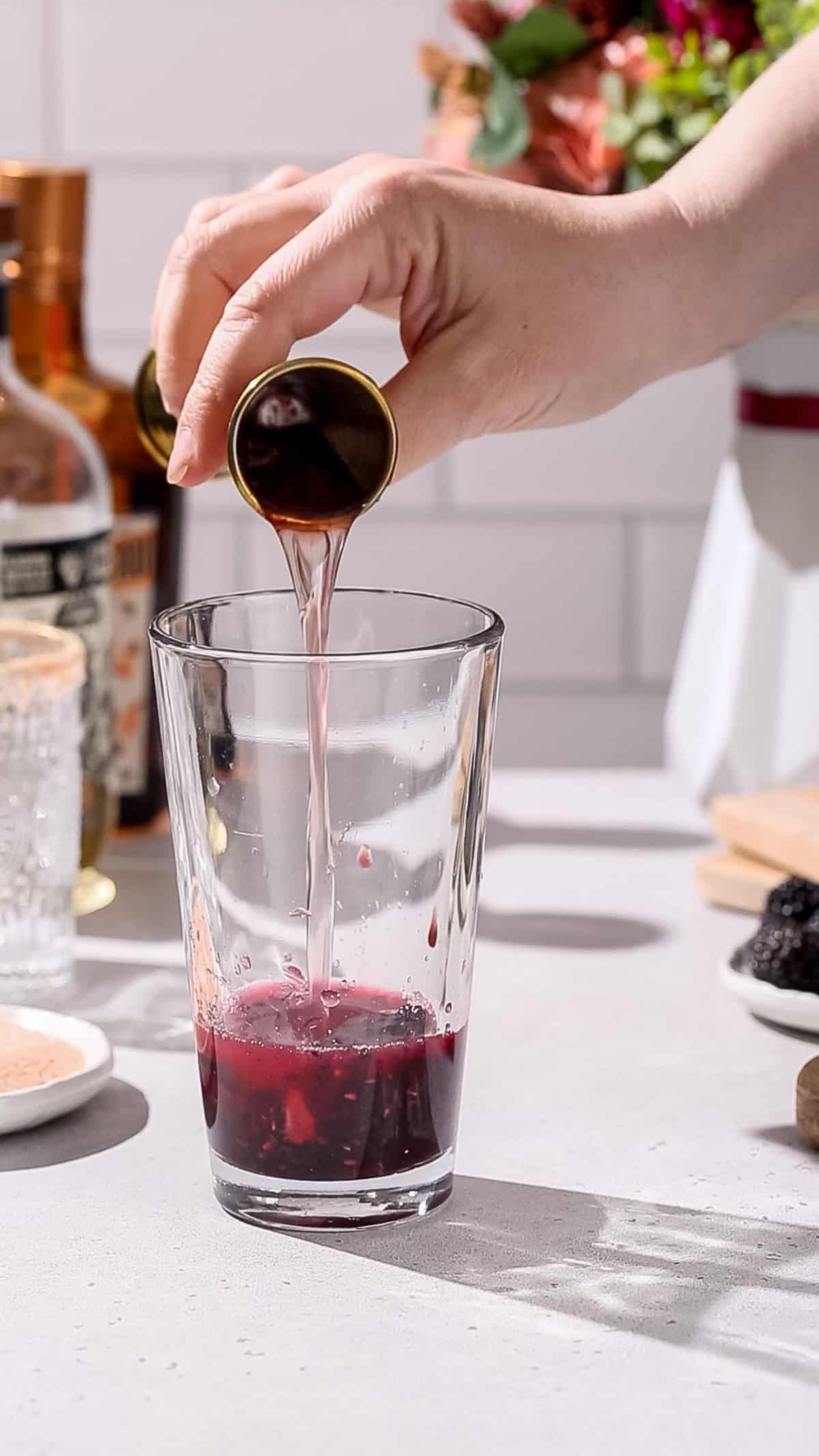 Hand pouring Cointreau into a cocktail shaker.