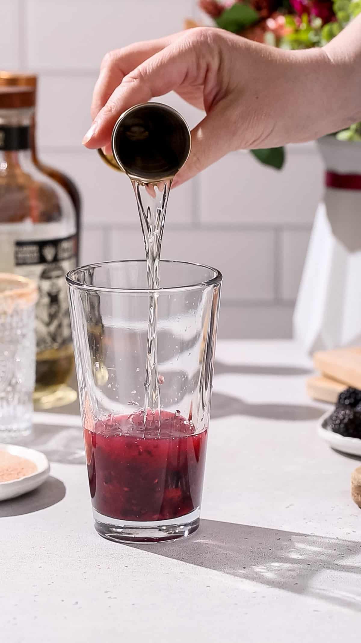 Hand pouring tequila into a cocktail shaker.