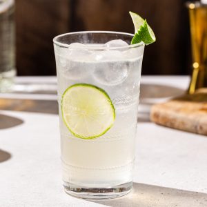 Side view of a Vanilla Lime Vodka Refresher cocktail with a lime wheel on the inside of the glass and a lime peel garnish on the rim of the glass.