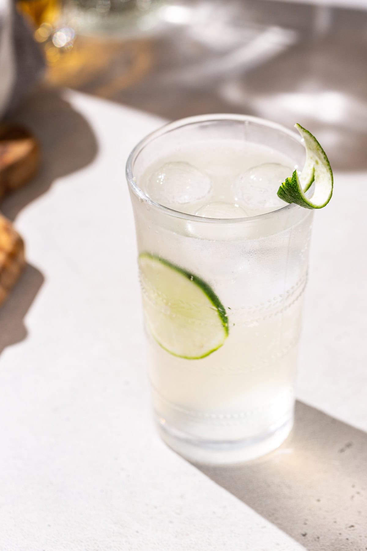 Overhead view of a Vanilla Lime cocktail with a cutting board in the background. The drink is garnished with a cut lime and a lime peel.