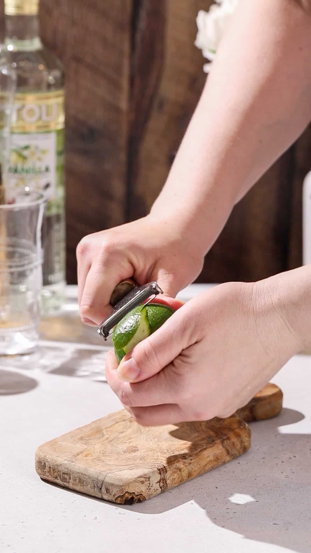 Hands using a vegetable peeler to peel a lime.