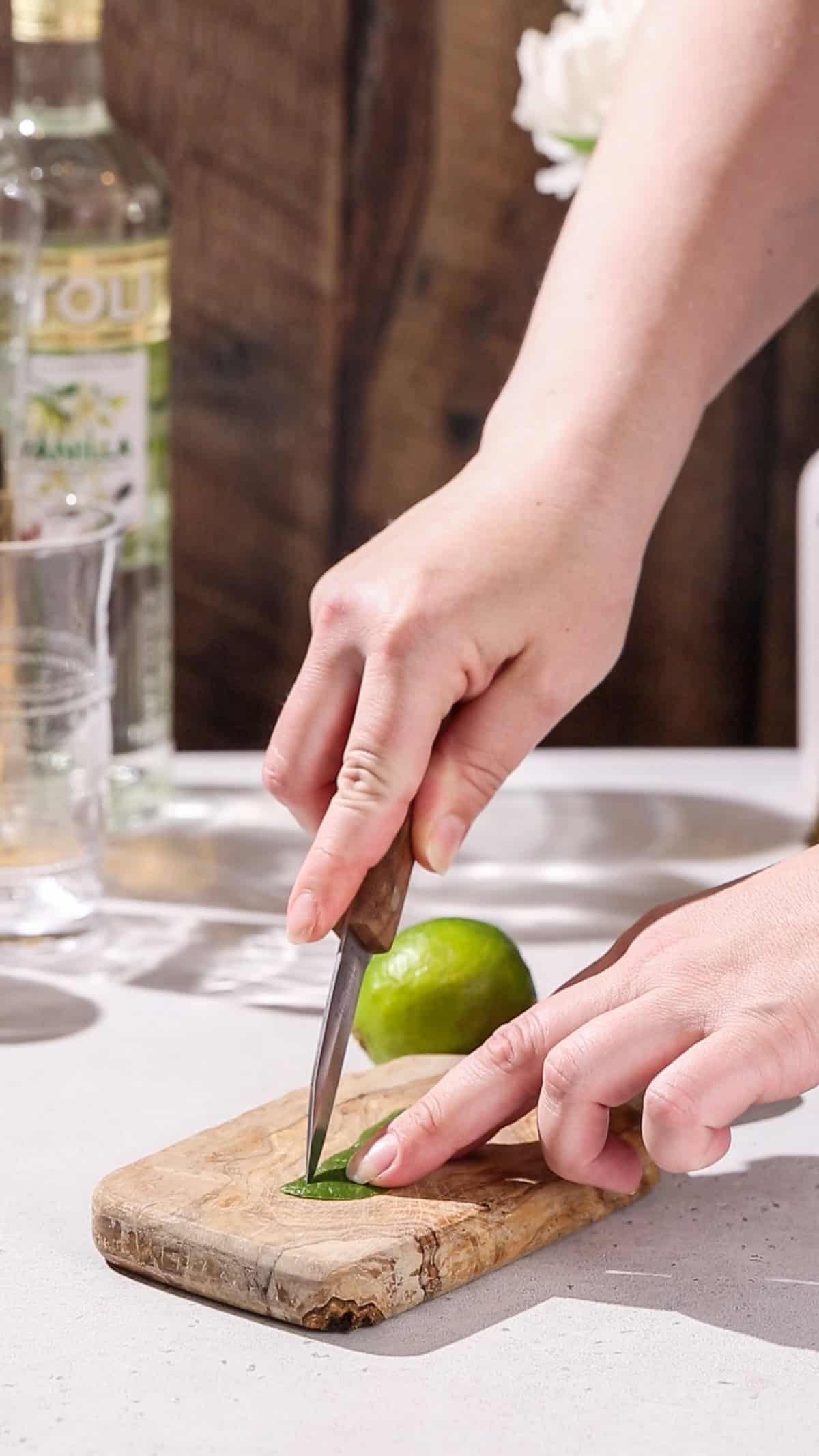 Hands cutting a lime peel into shape using a paring knife.