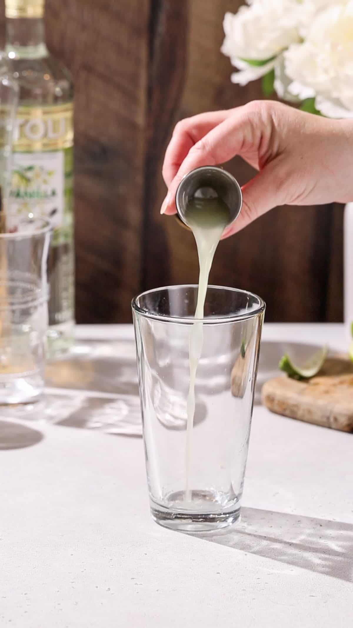 Hand pouring lime juice into a cocktail shaker.