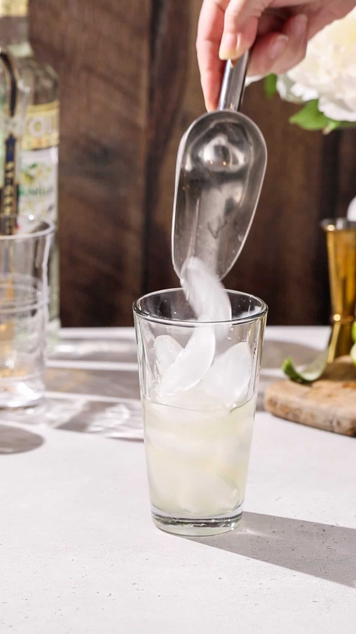 Hand filling a cocktail shaker with ice.