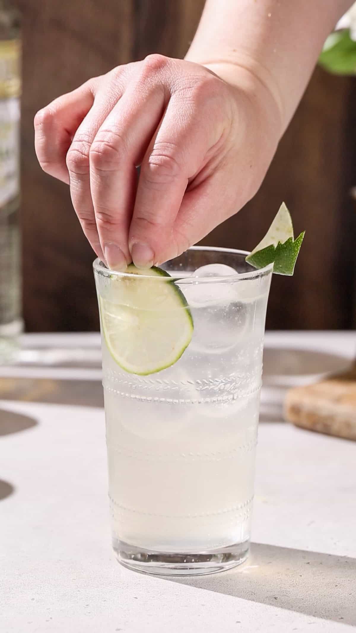 Hand adding a lime slice to the side of a cocktail.