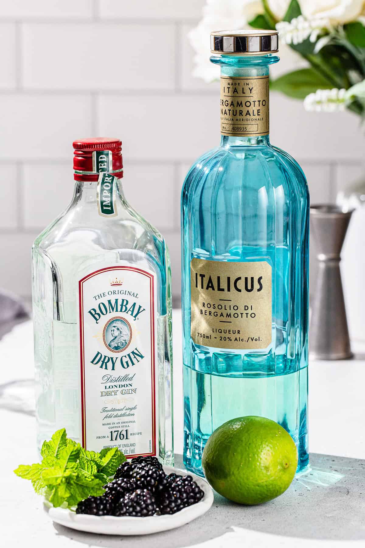 Ingredients to make a Blackberry Bergamot Gin Gimlet together on a countertop.