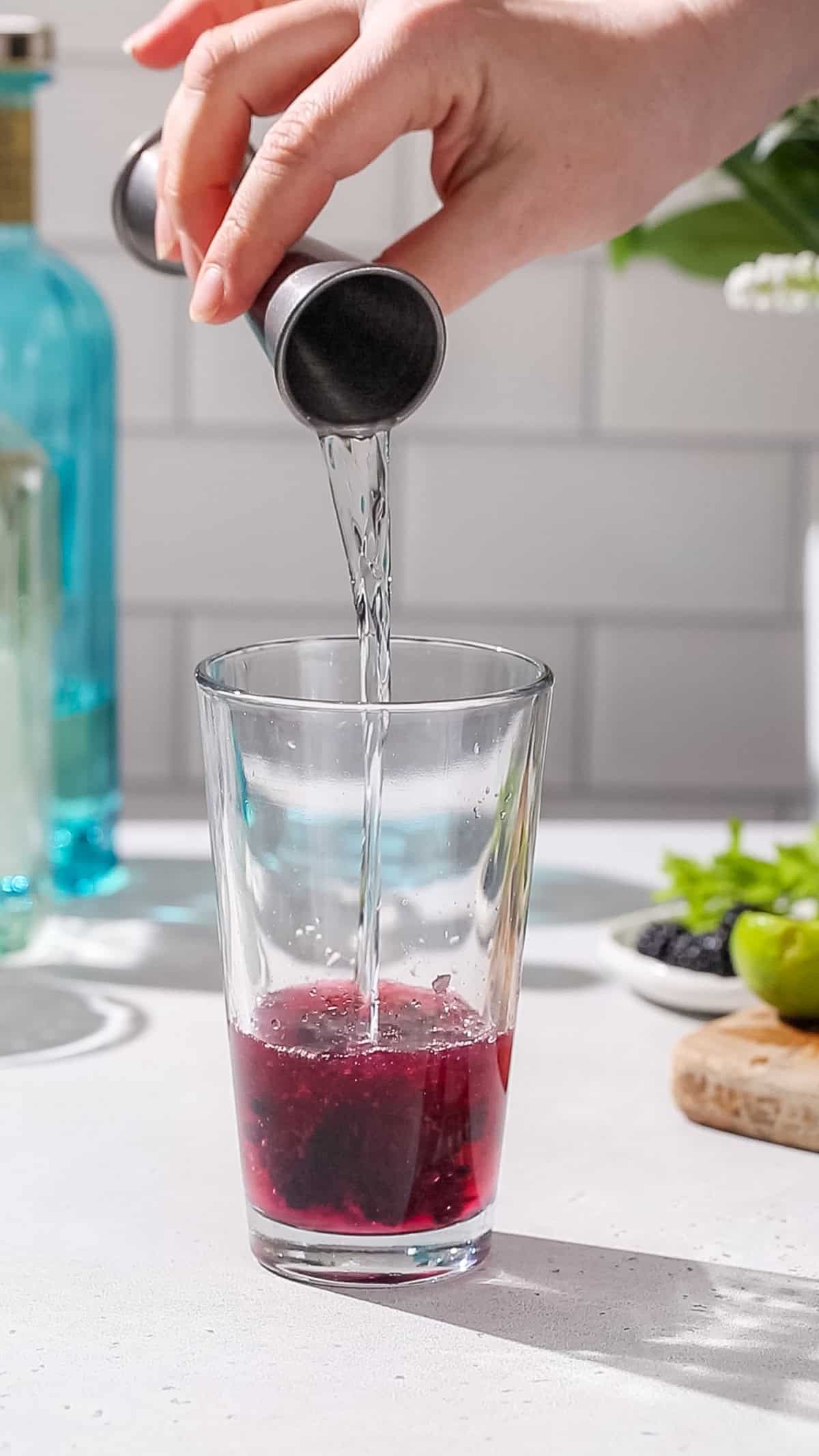 Hand pouring gin into a cocktail shaker.