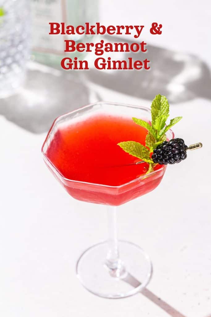 Overhead view of a red cocktail in a coupe glass with a fresh mint and blackberry garnish. Text above the drink says “blackberry bergamot gin gimlet” in red letters.