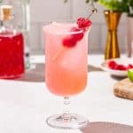 Side view of a pink colored Floradora gin cocktail. Bar tools and ingredients are in the background.