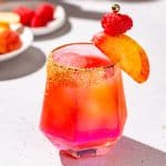 Side view of a Bourbon smash cocktail with fresh raspberry and peach.