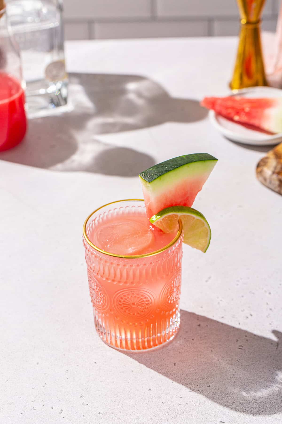 Overhead view of a Watermelon Paloma with a watermelon slice and lime slice as garnish. In the background are some fresh watermelon slices and other ingredients.