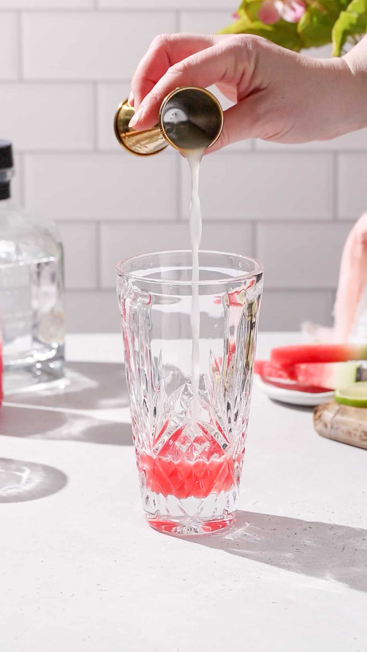 Hand pouring lime juice from a jigger into a cocktail shaker.