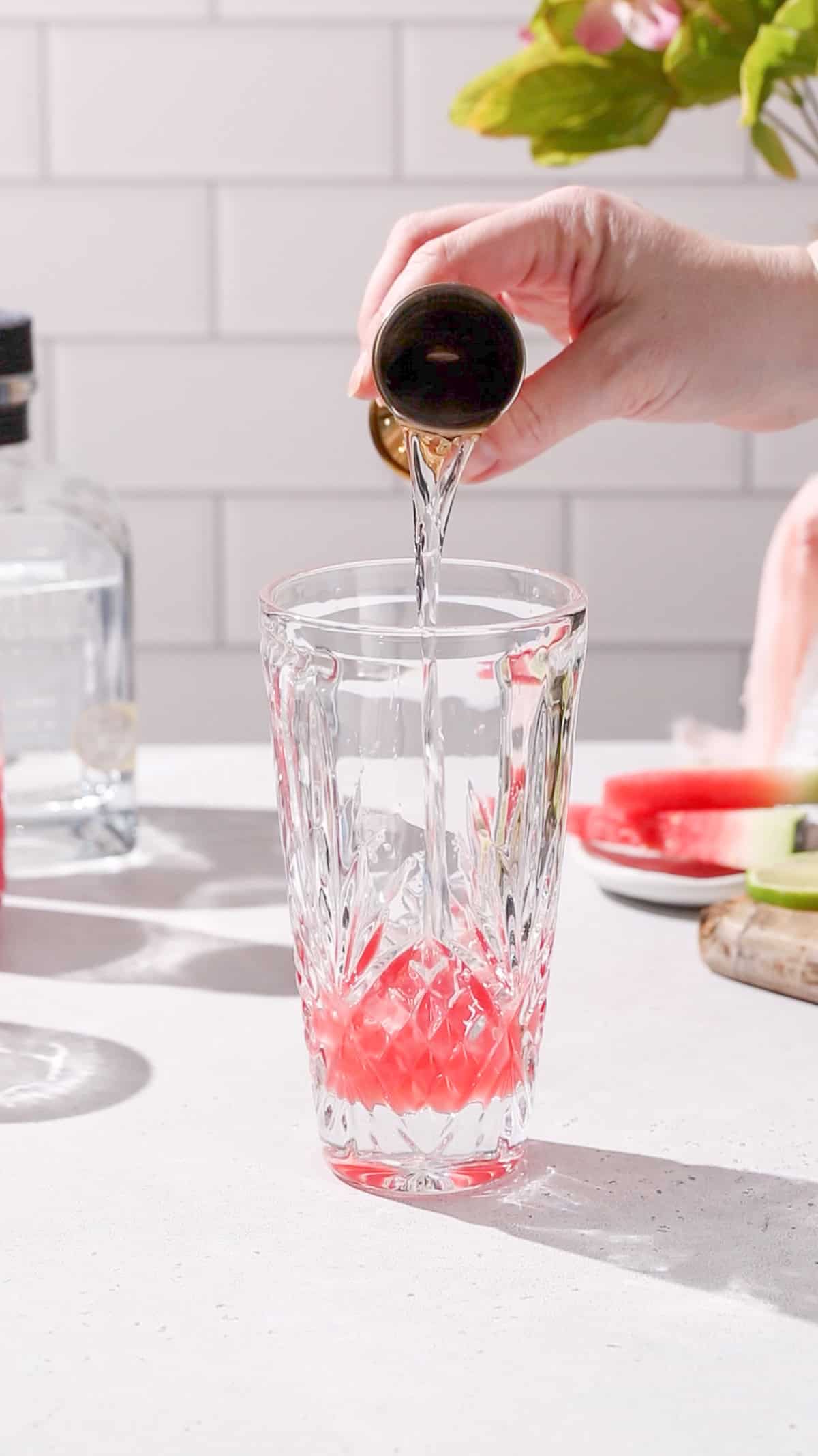 Hand pouring tequila from a jigger into a cocktail shaker.