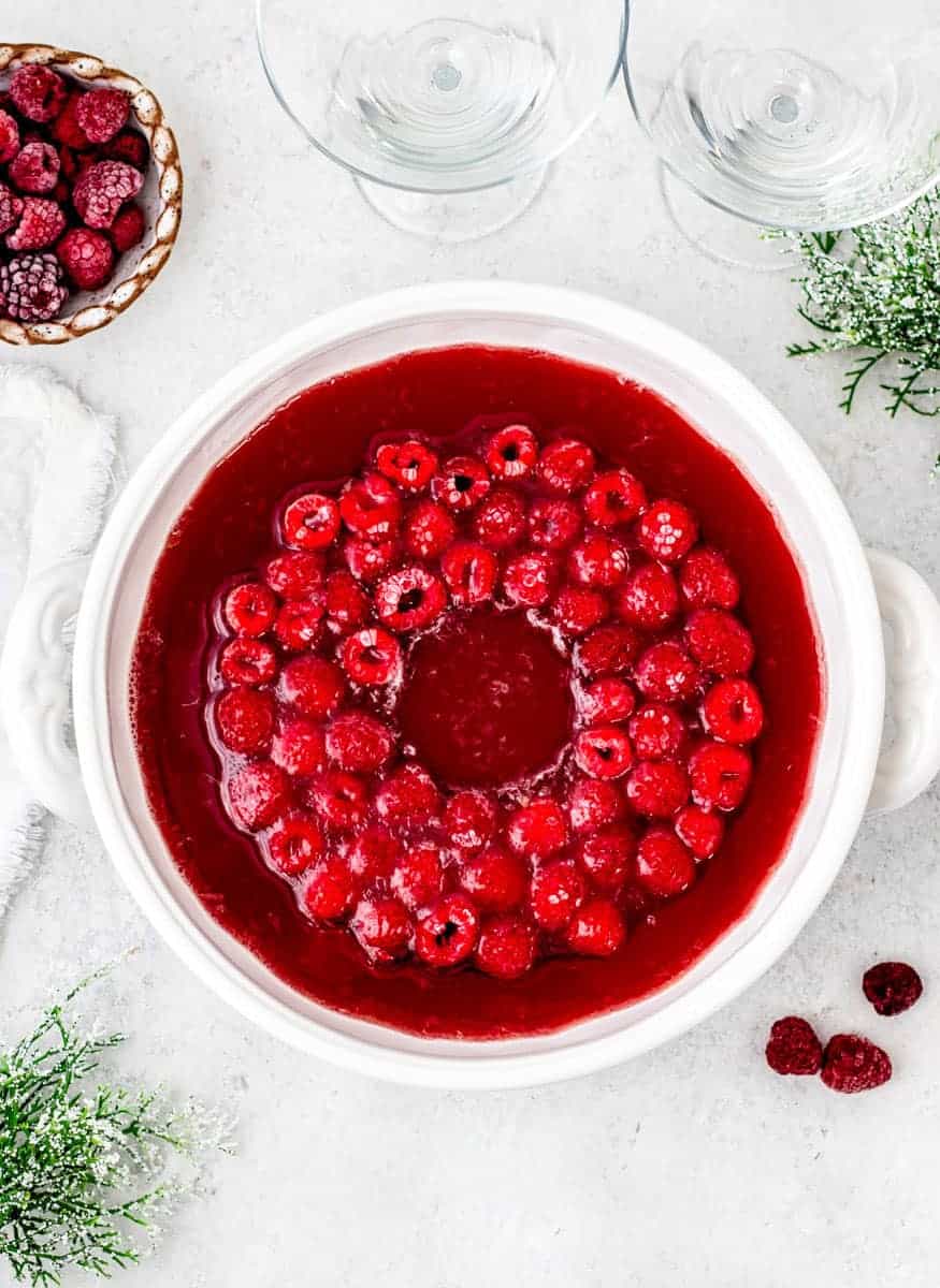 Overhead view of a punch bowl with red liquid inside. A ring of frozen raspberries is floating in the center of the bowl.