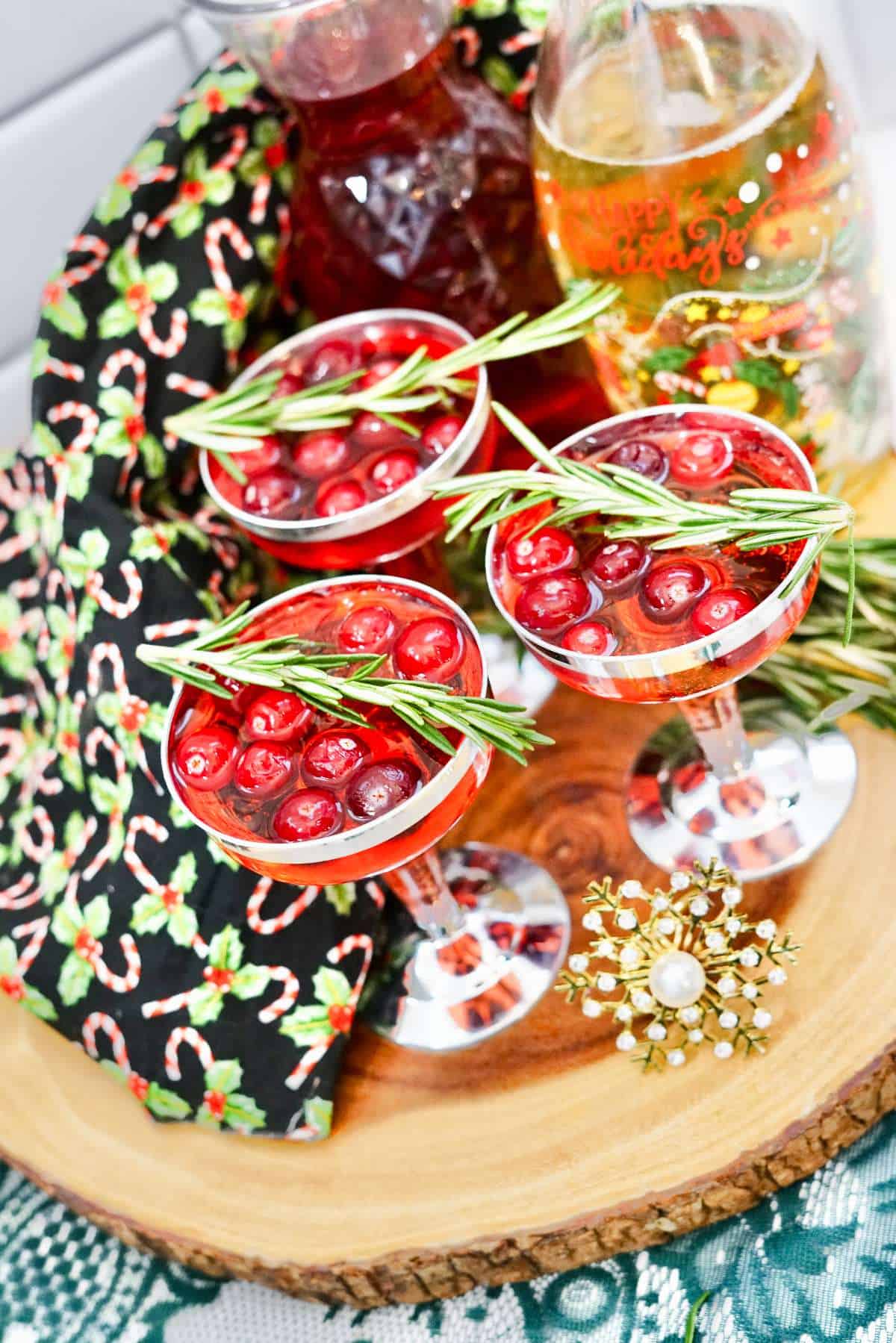 Overhead view of three champagne glasses filled with red liquid and garnished with cranberries and rosemary sprigs.